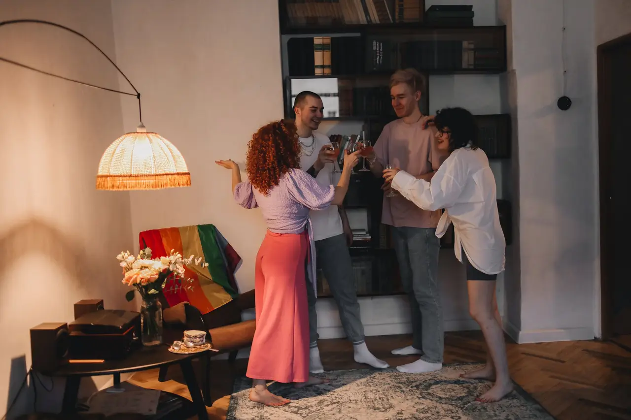 Friends raising their glasses at a party at home, a rainbow flag behind them.